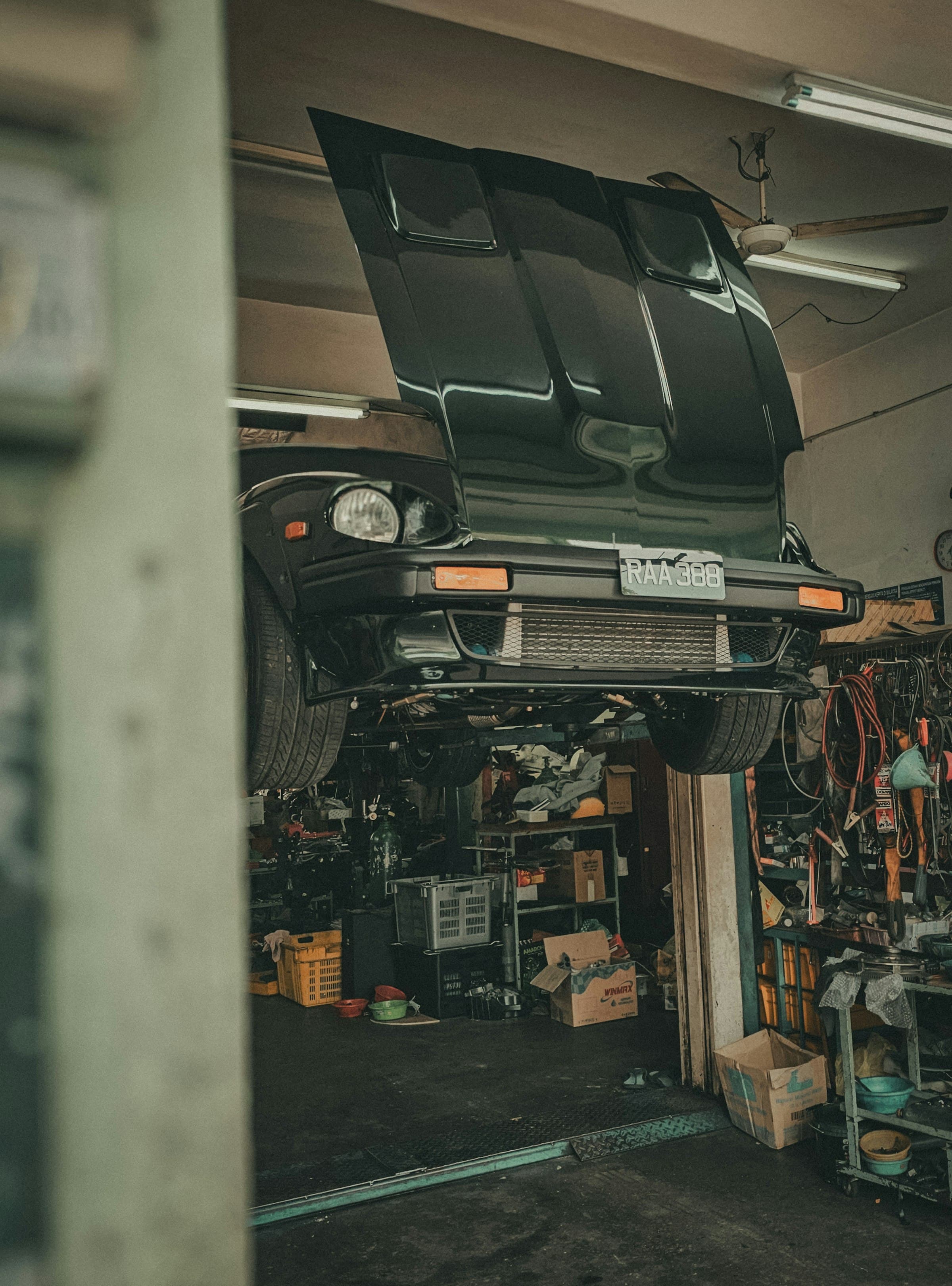 Car raised on a lift in a busy workshop, its bonnet open