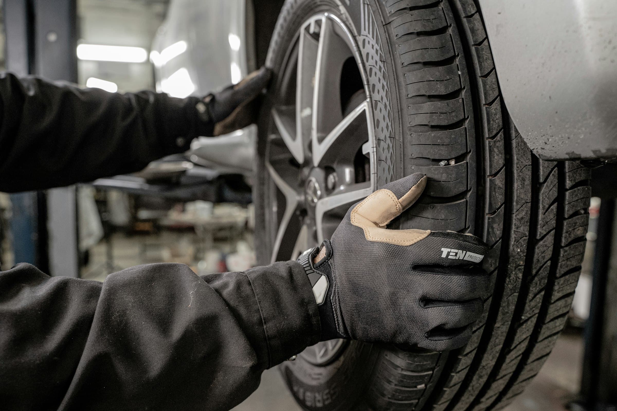 Gloved technician fitting a tyre to a car raised on a workshop lift