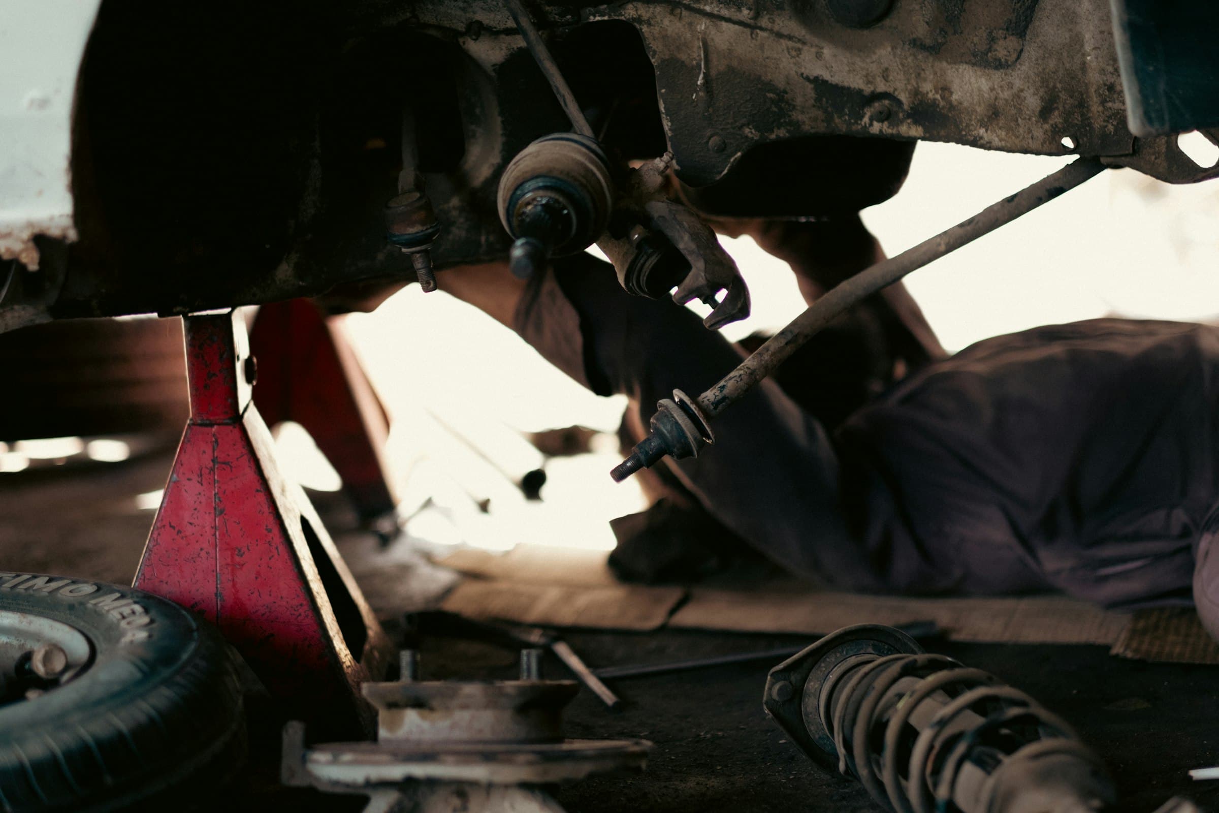 Technician working beneath a raised car, beside red axle stands